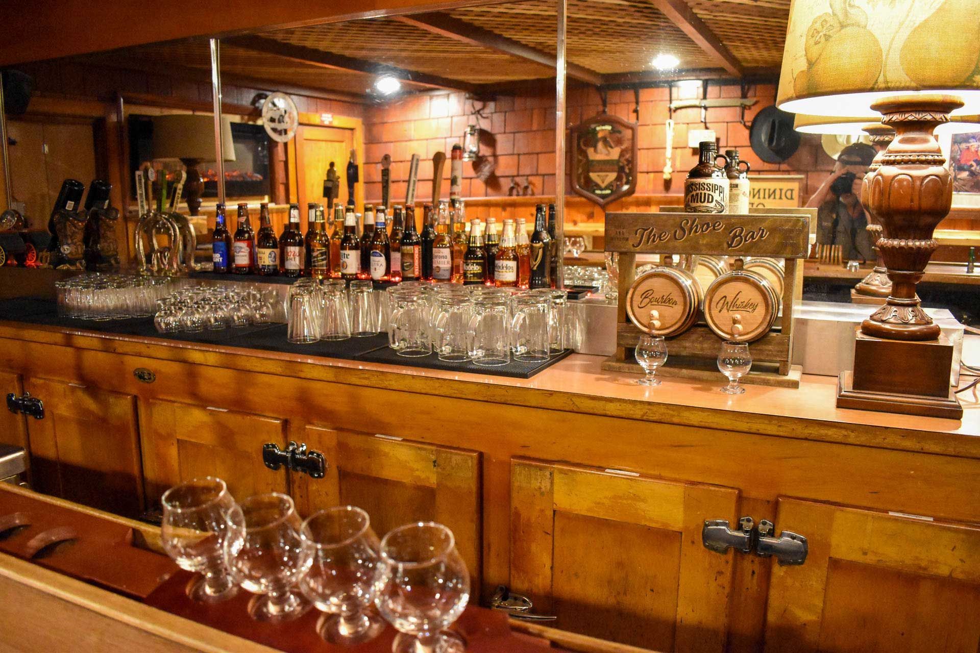 Warm wooden bar interior with glassware, liquor bottles, and vintage clocks on the counter.