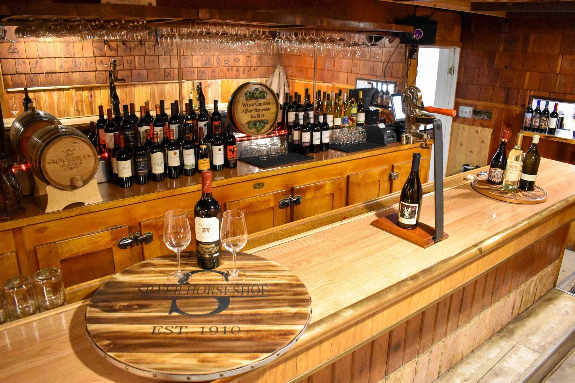 Wine bar counter with bottles, wine barrels, and glasses in a rustic wooden cellar