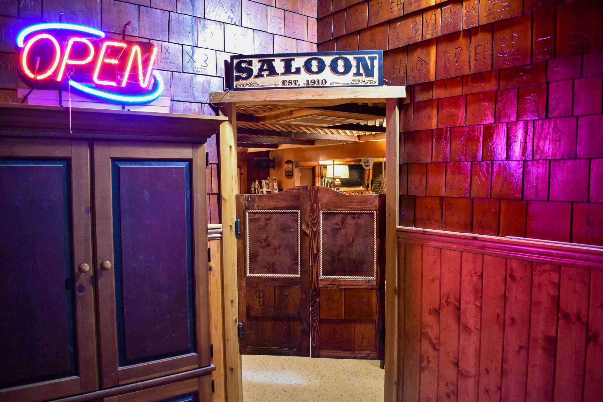 Neon “OPEN” sign above a saloon doorway with wooden doors and warm interior light