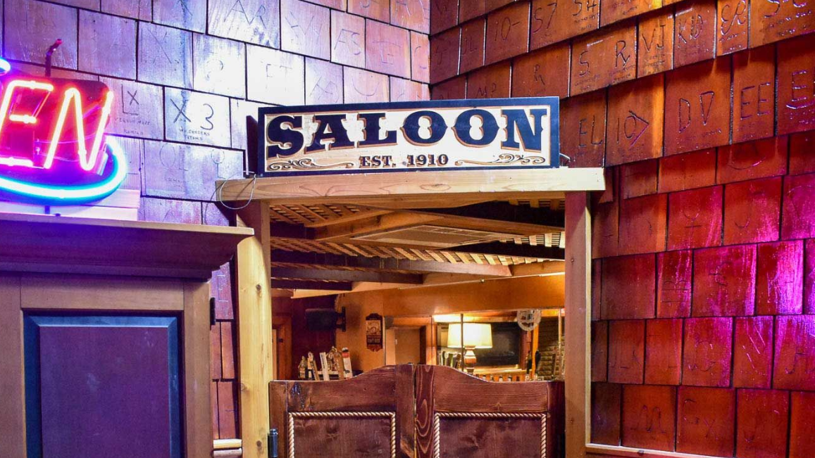 Neon-lit saloon entrance with wooden doors and a large “SALOON” sign above the doorway