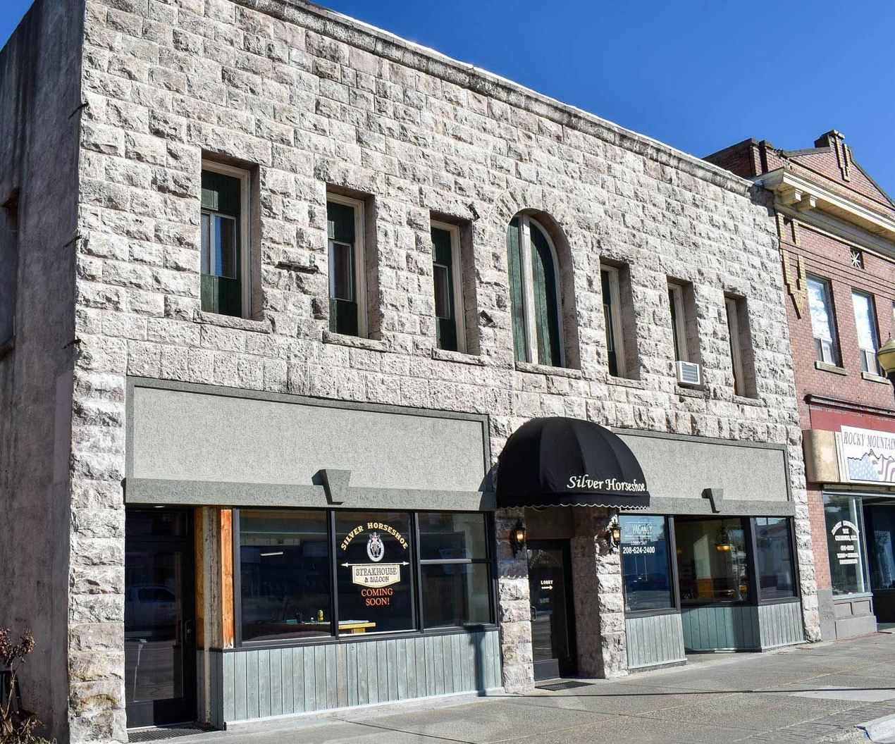 Stone storefronts with a black awning on a sunny street corner