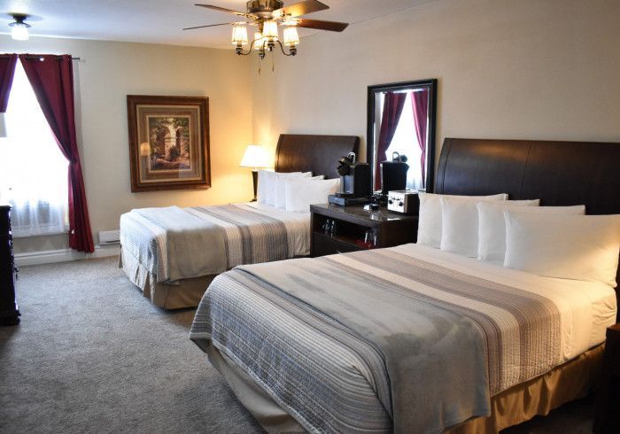 Hotel room with two beds, white bedding, dark headboards, and a ceiling fan near the window.