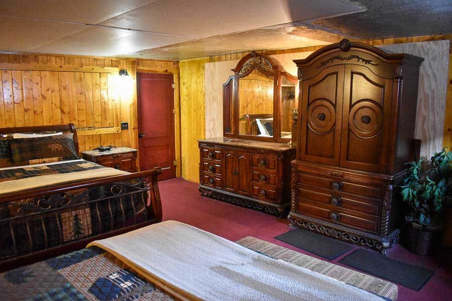 Wood-paneled bedroom with antique wooden furniture, a bed, red door, mirror, and wardrobe.