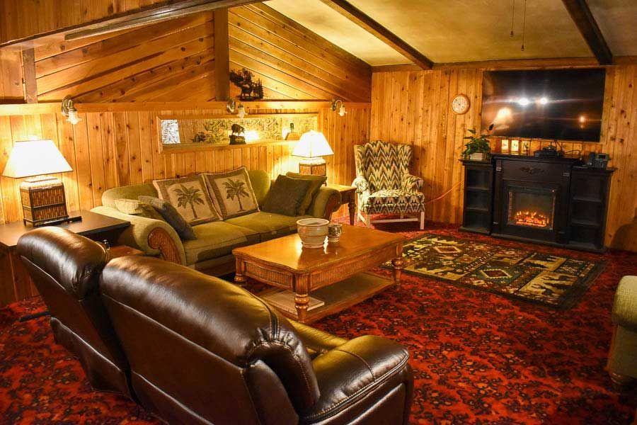 Cozy wood-paneled cabin living room with leather sofa, armchairs, fireplace, and patterned rug