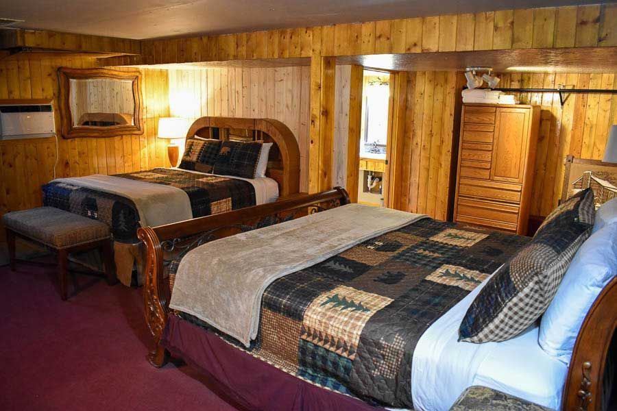 Wood-paneled bedroom with two beds, warm lighting, and a red carpeted floor