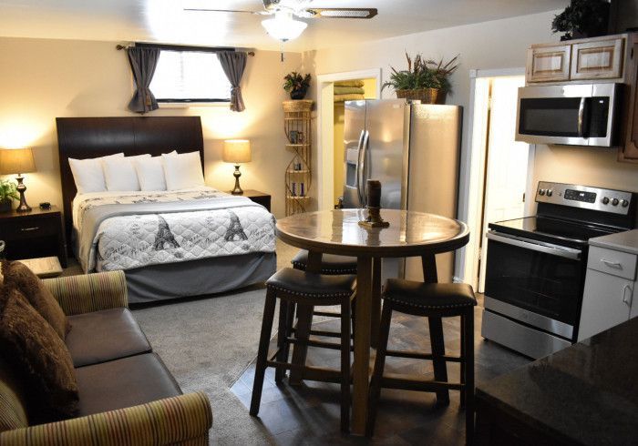 Small studio apartment with bed, sofa, kitchen, and round dining table in warm lighting