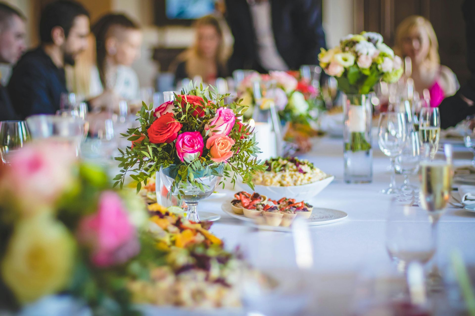 Flower-decorated banquet table with wine glasses and plates at a blurred reception event