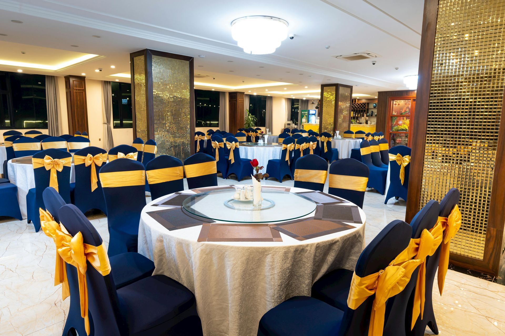 Elegant banquet hall with round tables, navy chairs with gold bows, and mirrored gold columns