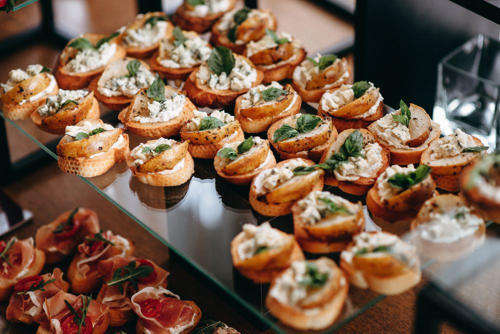 Aperitivos en vitrina: rodajas de pan tostado coronadas con diversos ingredientes y guarnición de albahaca.
