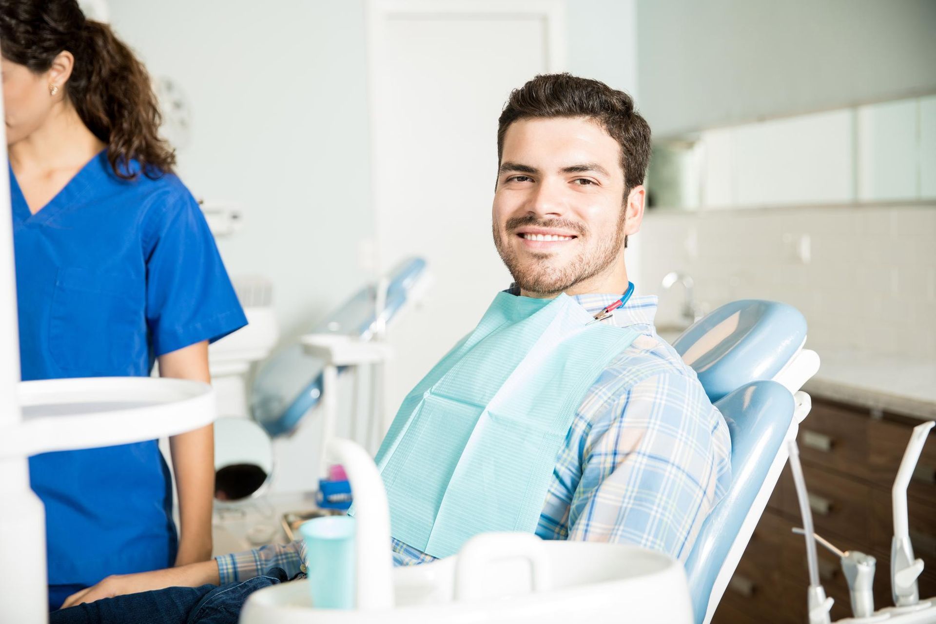 Man smiling in a dental chair with a dentist in blue scrubs nearby, clinic setting