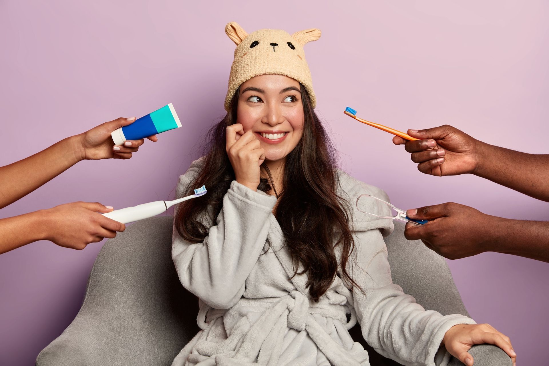 Woman smiling in chair while multiple hands hold grooming tools around her on a pink background