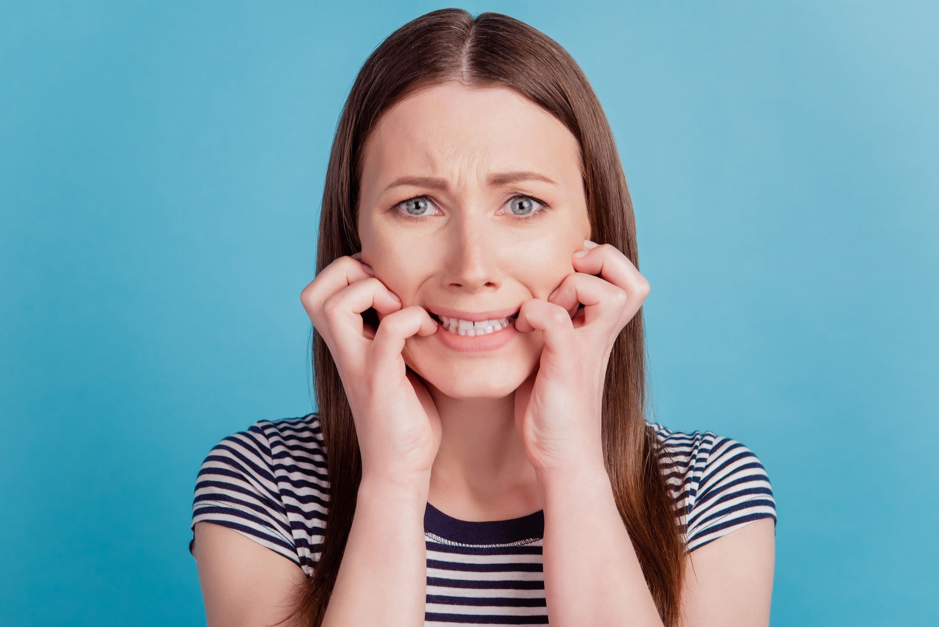 Person grimacing and pulling their cheeks with both hands against a blue background