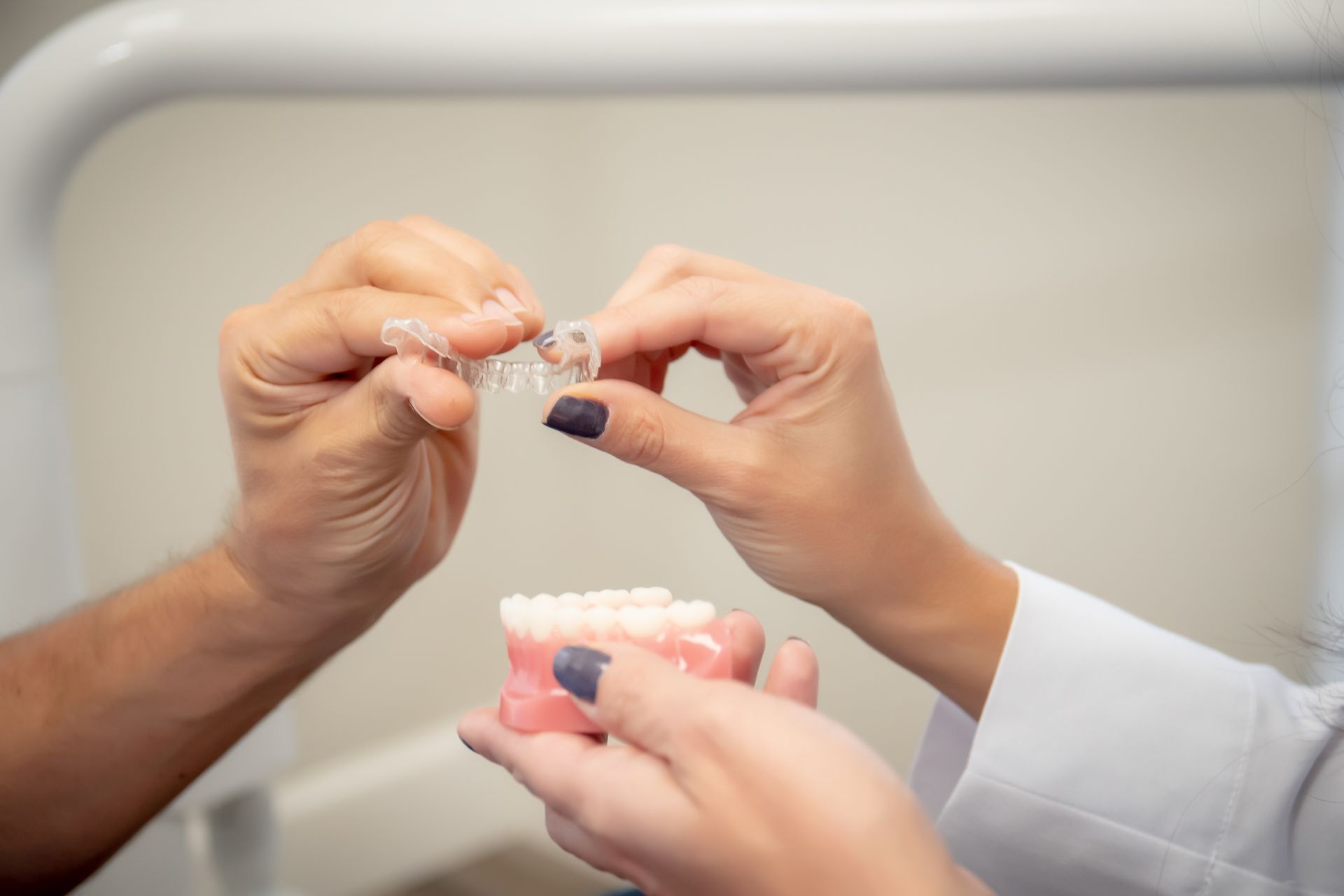 Hands fitting clear orthodontic aligners over a model of teeth in a clinical setting