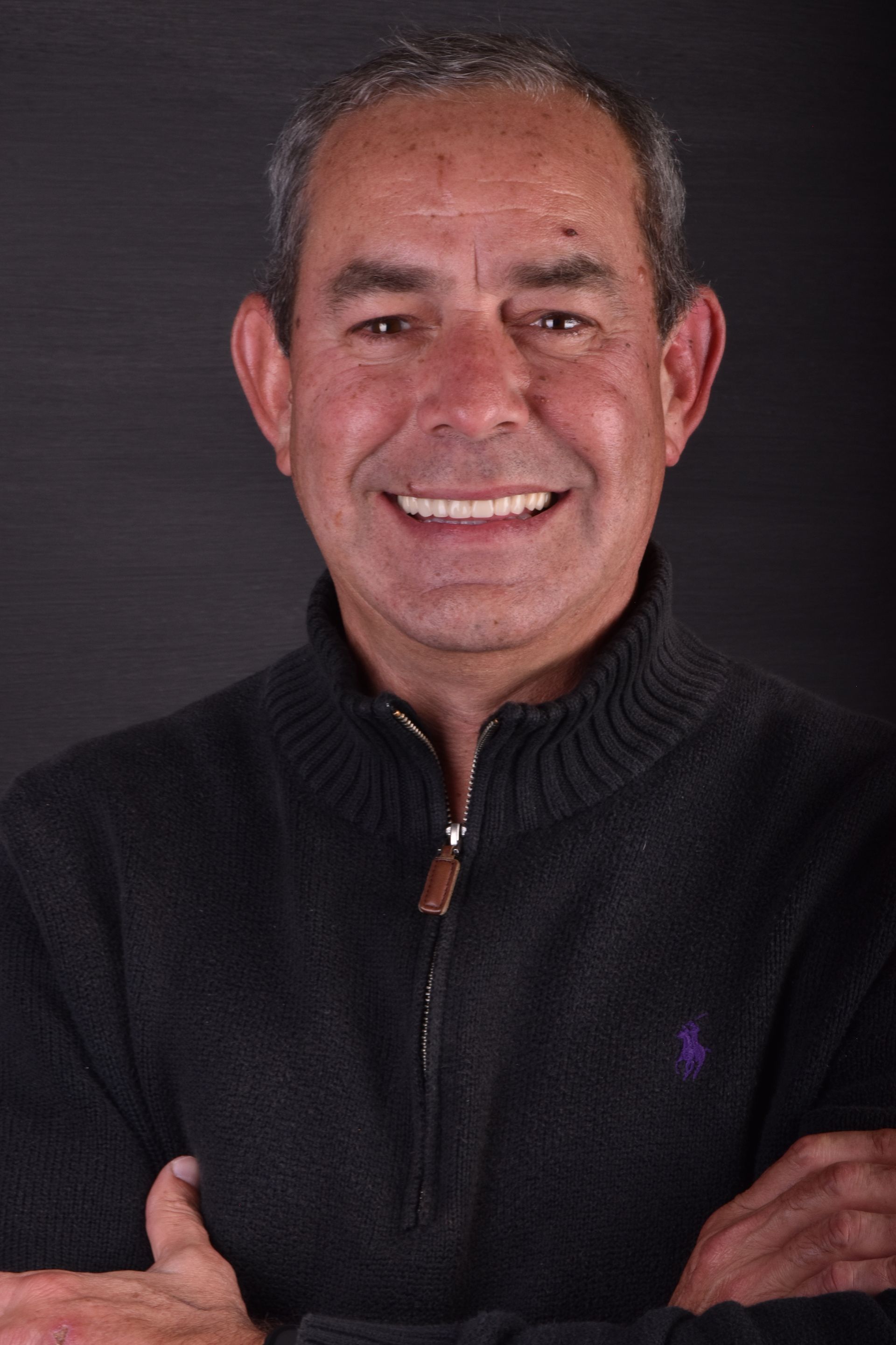 Smiling man with short gray hair against a dark background