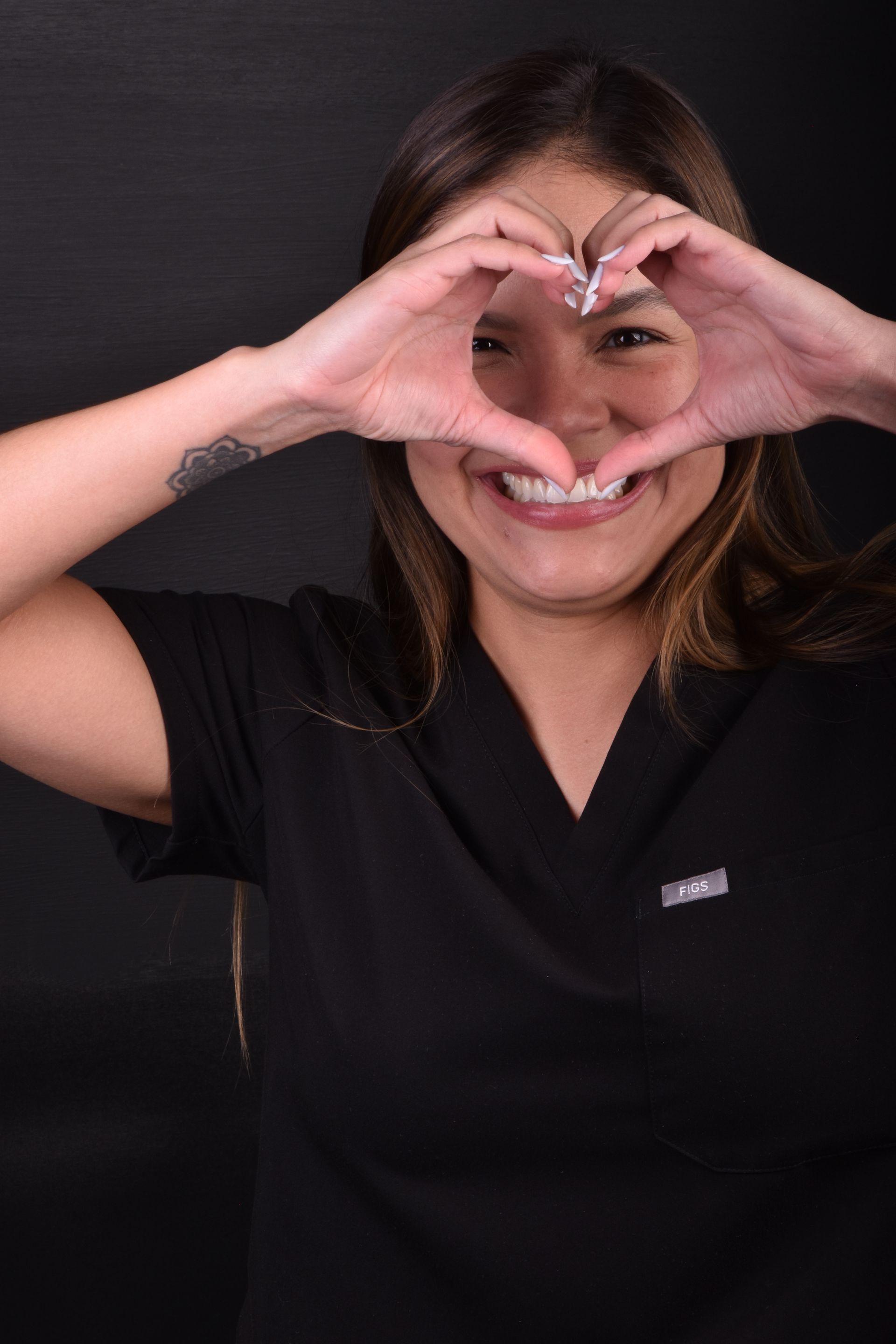Smiling woman in black shirt making a heart shape with her hands over her face