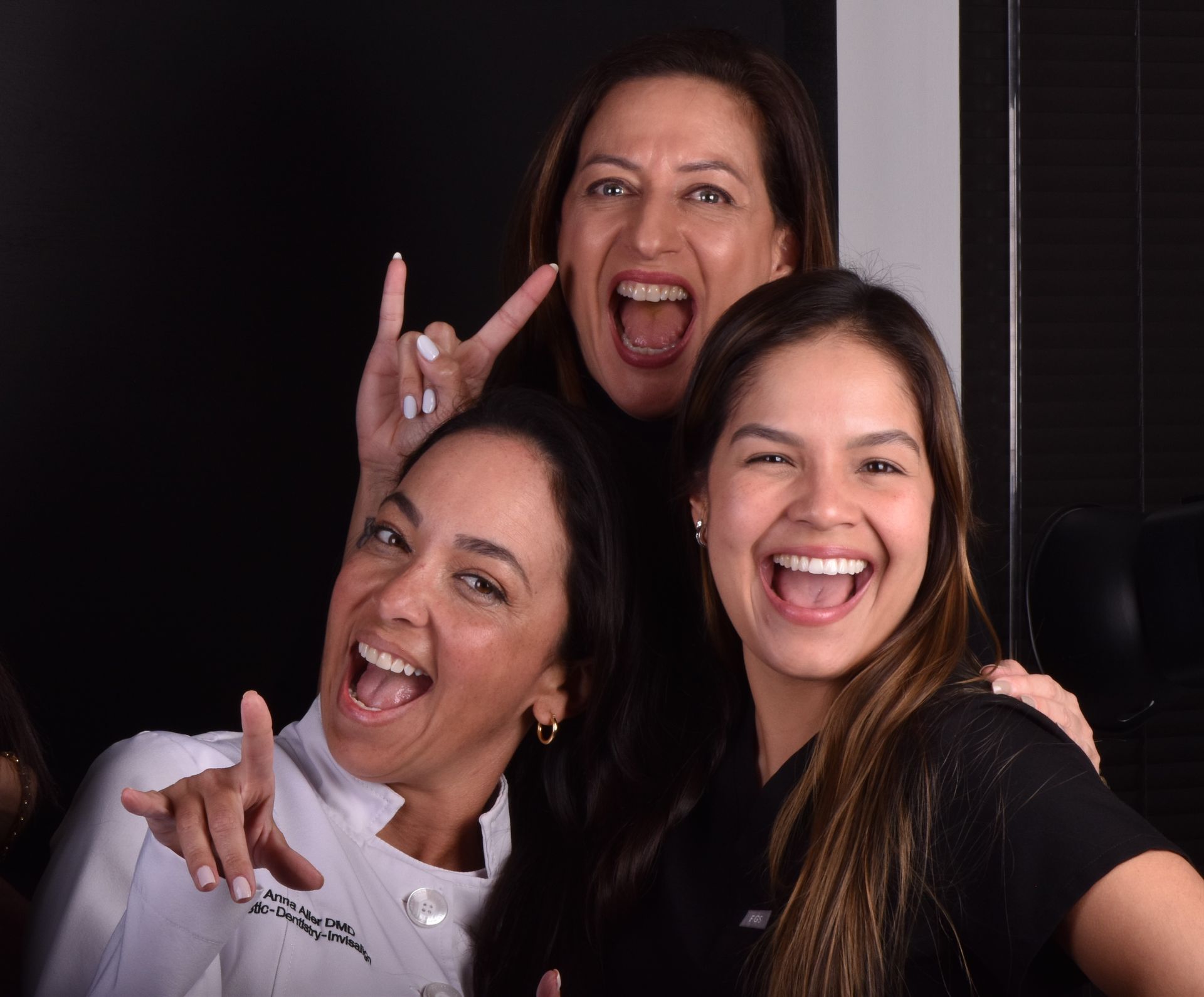 Three smiling people posing together, with one in back making playful horns behind the others.
