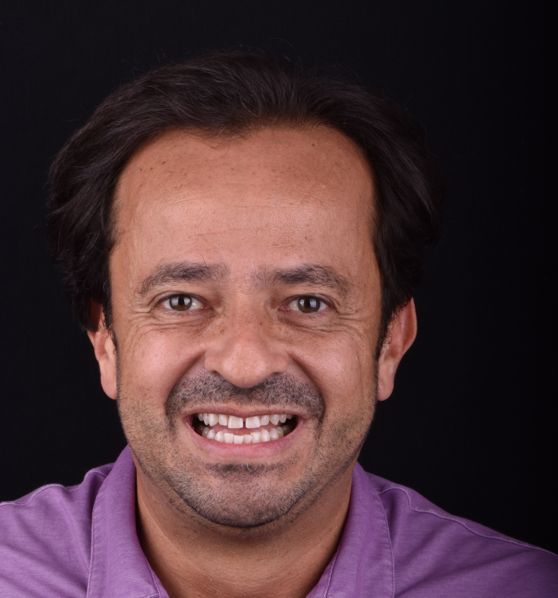Smiling man in a purple shirt against a dark background