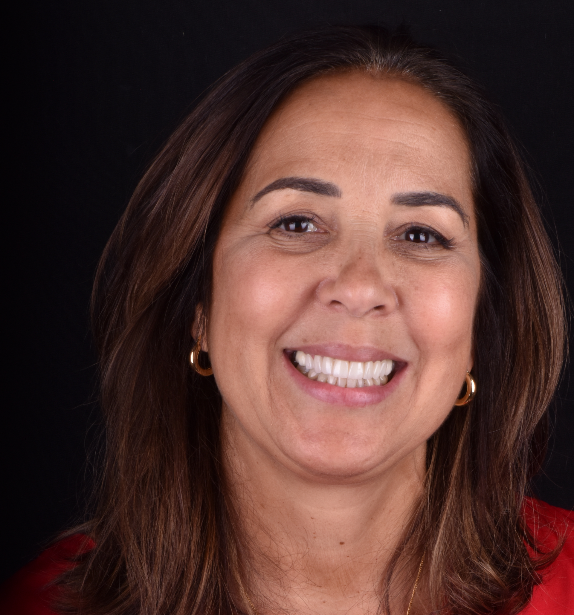 Smiling woman with shoulder-length brown hair against a dark background, wearing a red top.