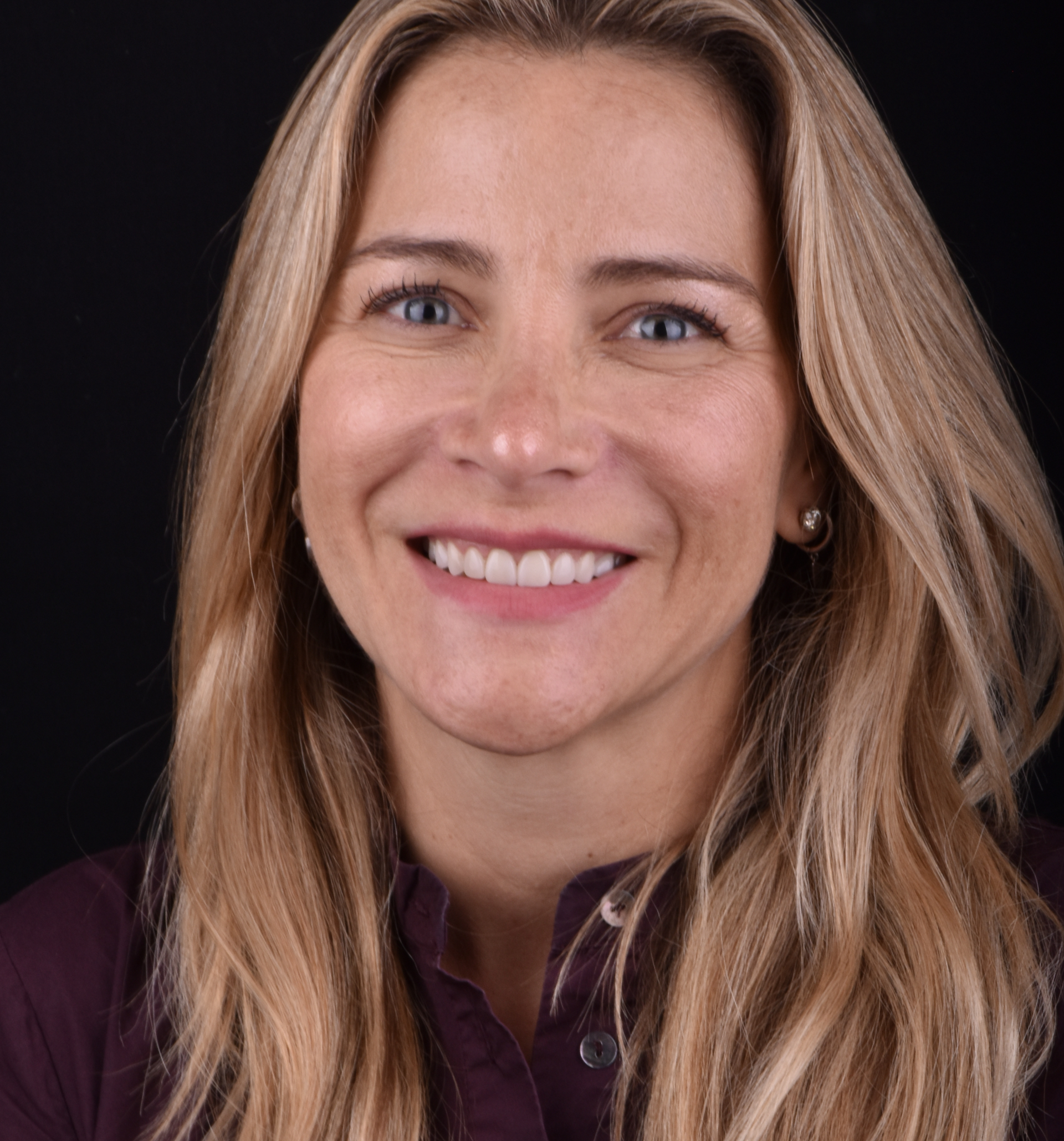 Smiling woman with blonde hair in a maroon shirt against a dark background