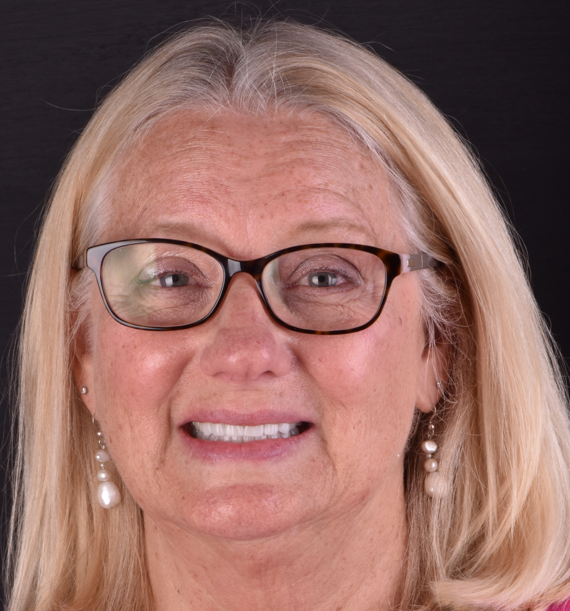 Smiling woman with blonde hair and glasses against a dark background