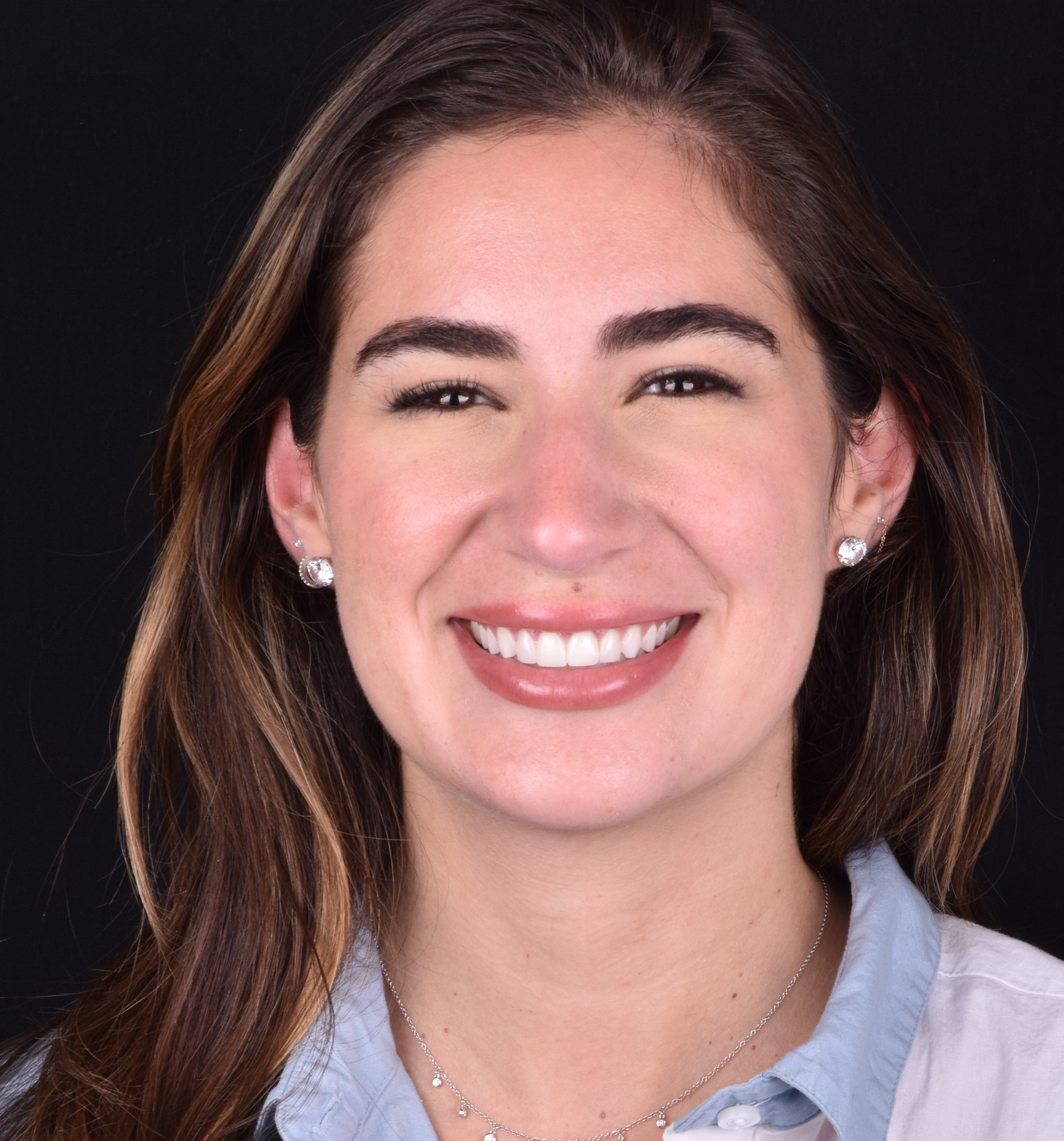 Smiling woman with short brown hair against a black background, wearing a light blue shirt and white cardigan