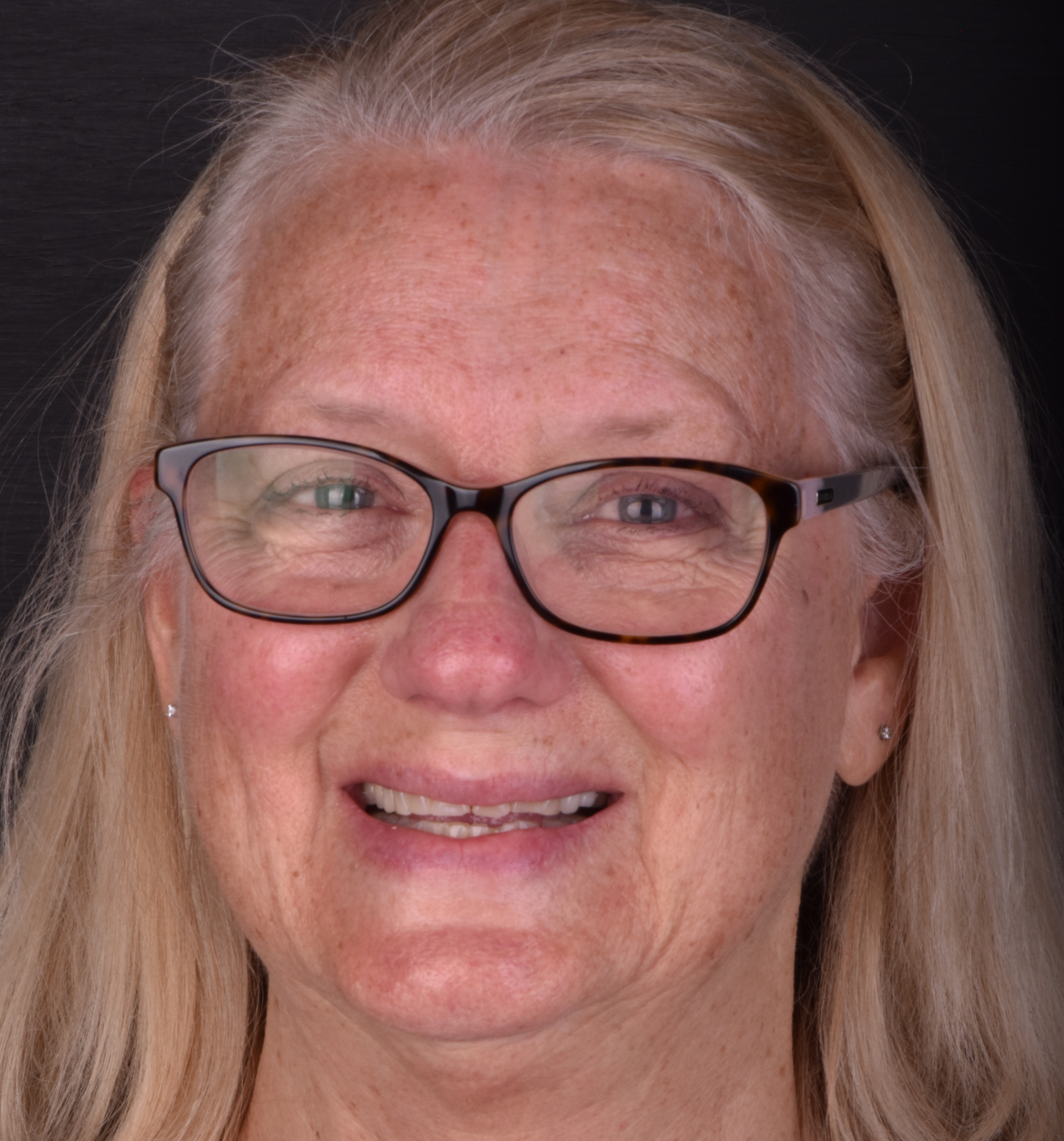 Smiling woman with glasses and long gray hair against a dark background