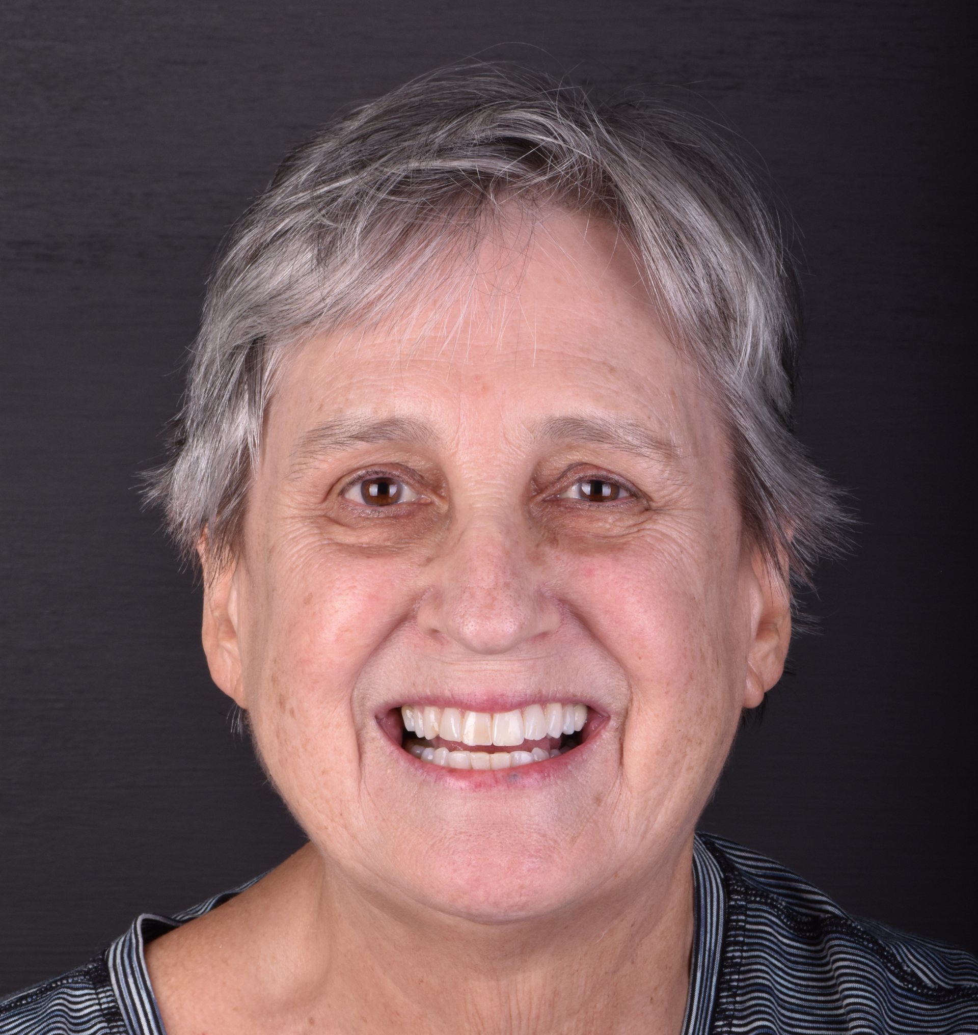 Smiling person with short gray hair on a dark background
