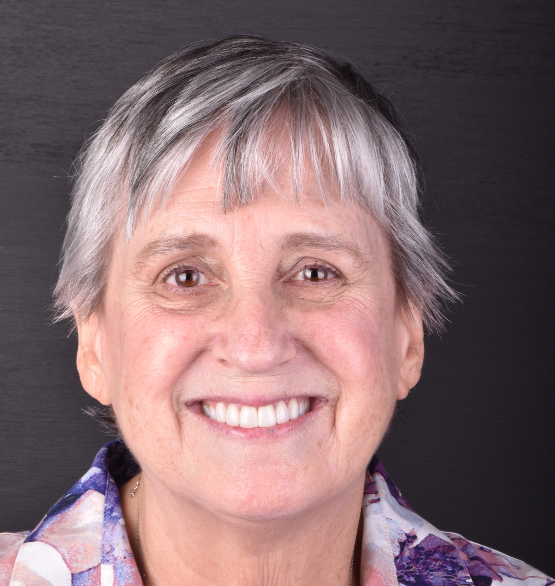 Smiling person with short gray hair against a dark background