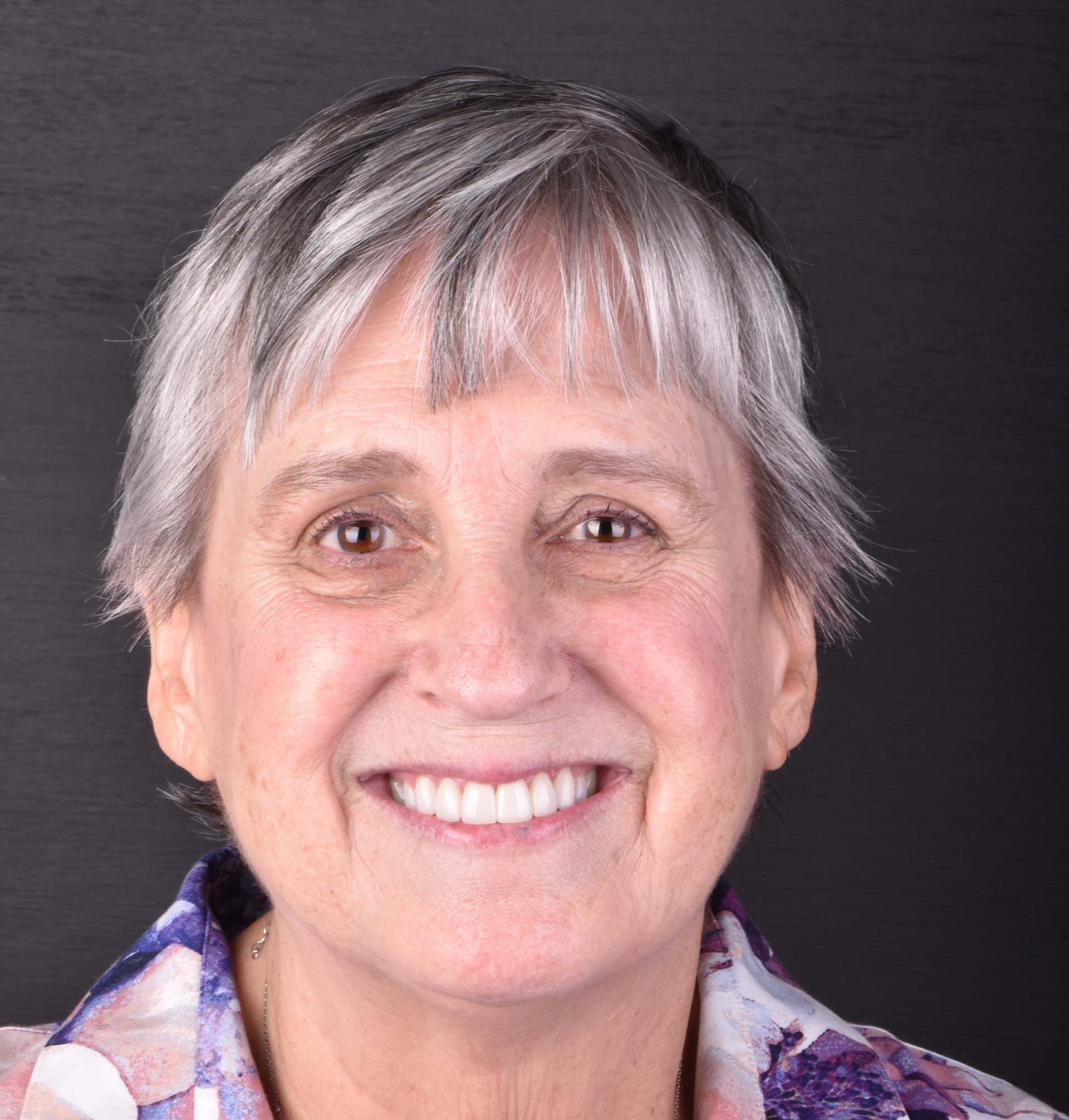 Smiling person with short gray hair against a dark background