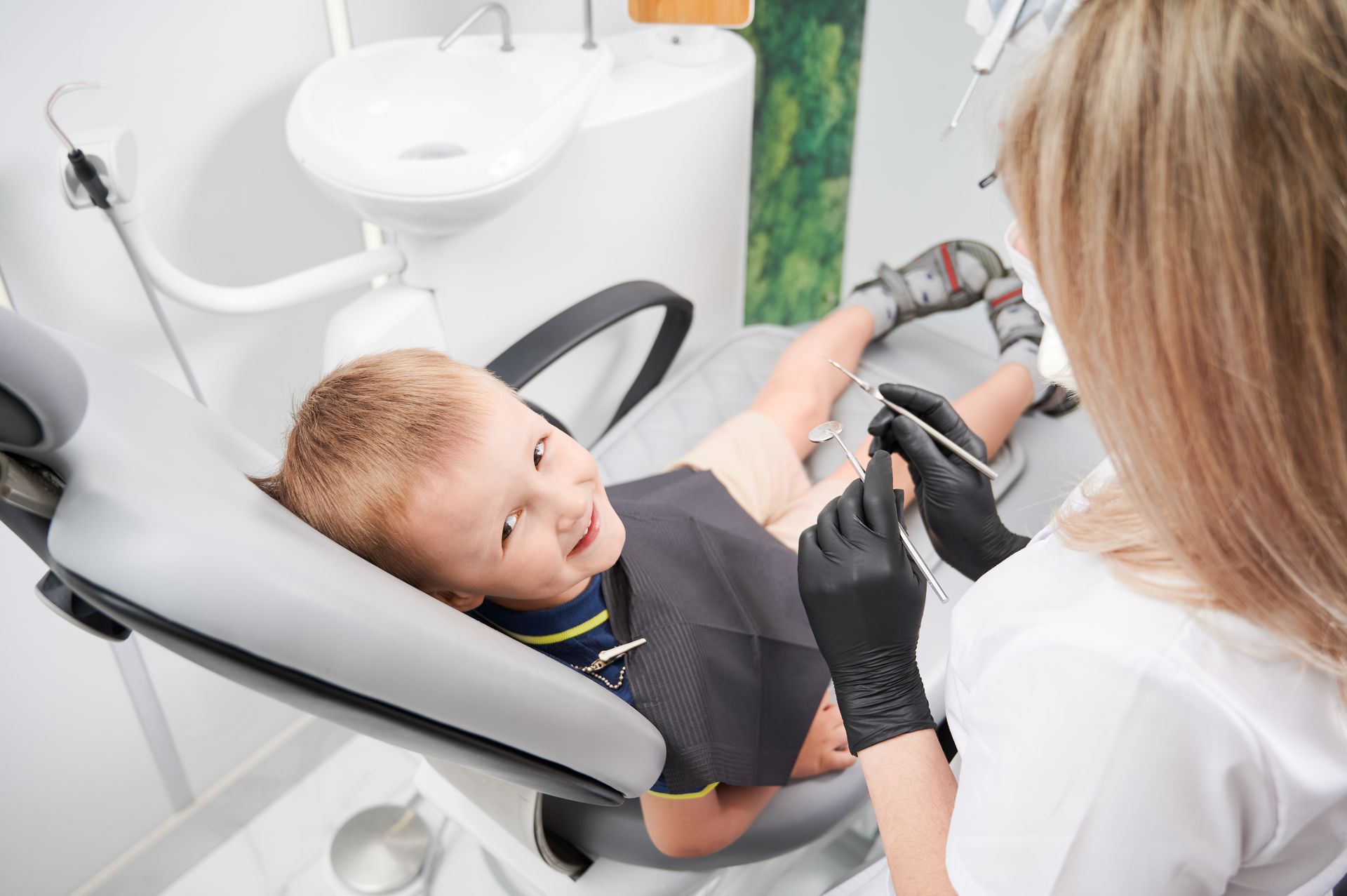 Child receiving dental treatment in a clinic while dentist works with tools beside the chair