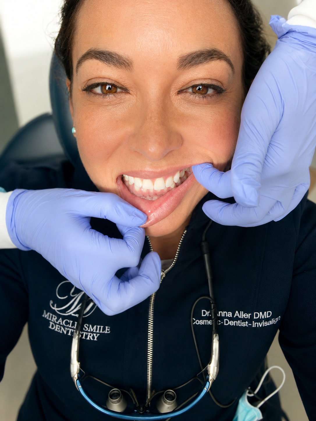 Dentist examining a smiling patient’s teeth with gloved hands in a dental clinic