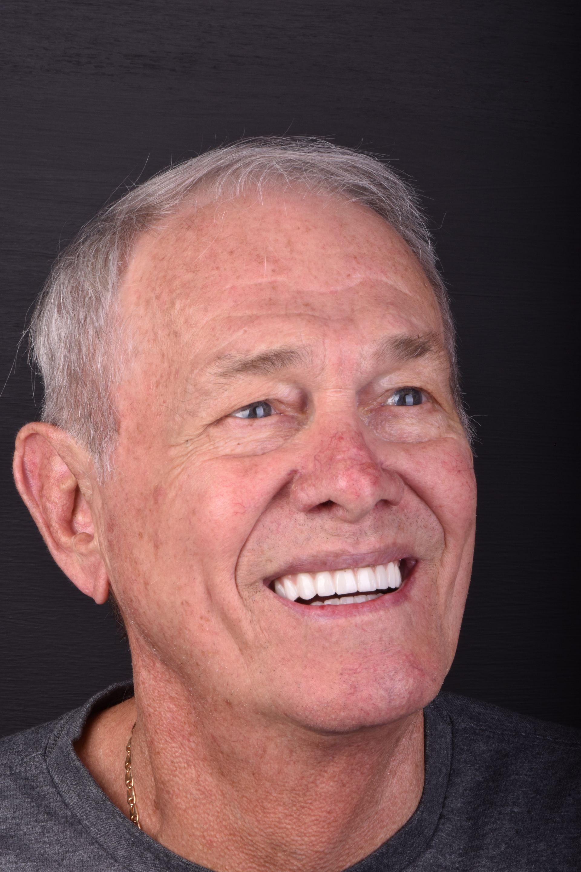 Smiling older man with short gray hair against a dark background