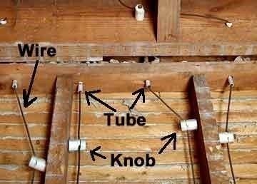 Vintage knob-and-tube electrical wiring consisting of wires, ceramic insulators, and ceramic tubes running along wood beams.