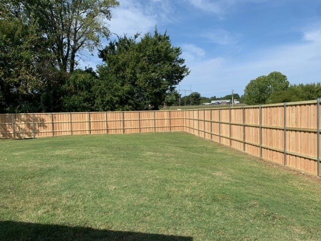 A wooden fence surrounds a lush green yard.