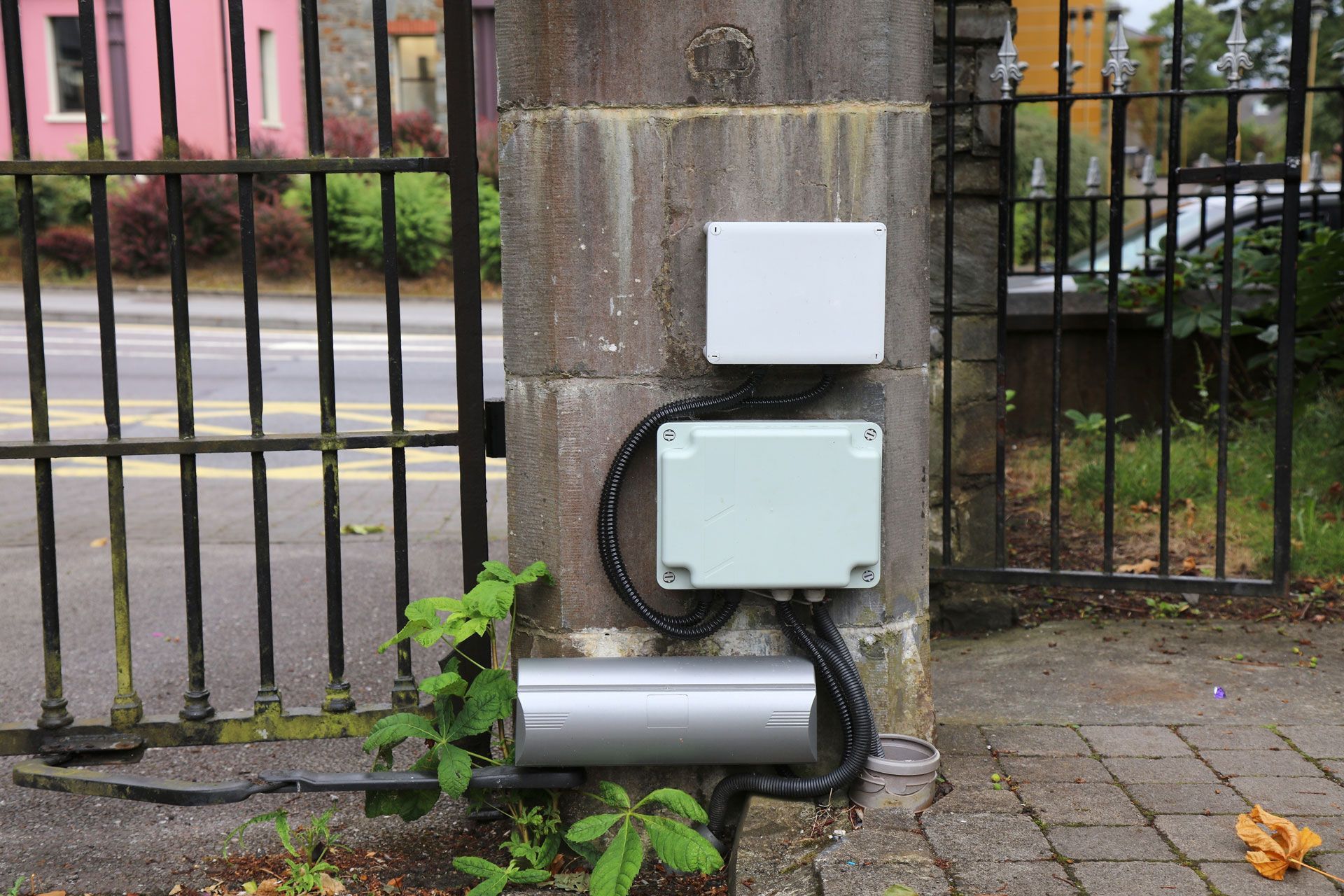 Two white boxes are sitting on a brick wall next to a gate.