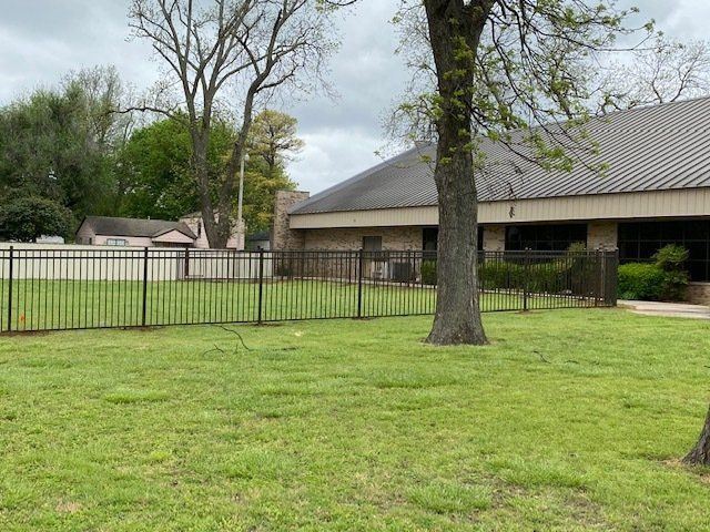 A large lawn with a fence and a tree in front of a house.