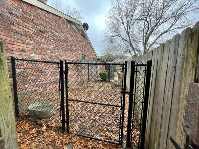 A chain link fence is surrounded by leaves and a wooden fence.