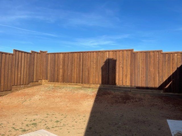 A wooden fence in a backyard with a blue sky in the background.