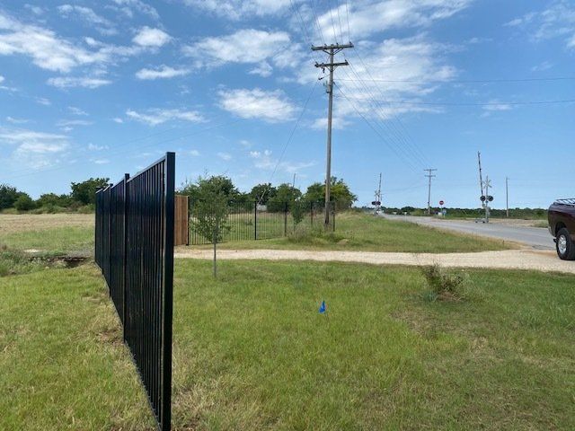 A black fence surrounds a grassy field next to a road.