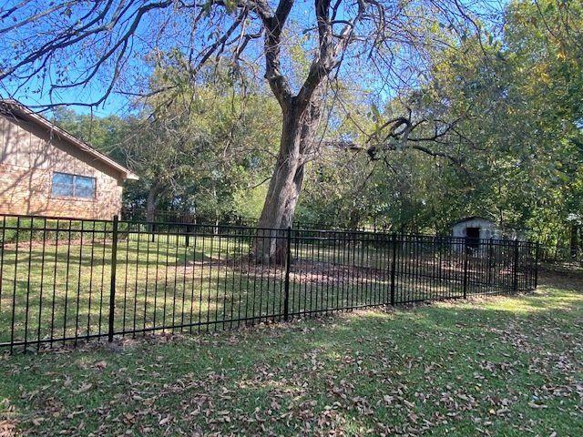 A black fence surrounds a lush green yard with a house in the background.
