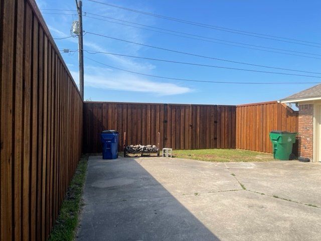 A wooden fence surrounds a concrete driveway in a backyard.