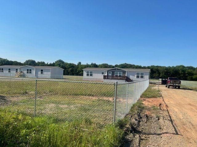 A chain link fence surrounds a house and a dirt road.