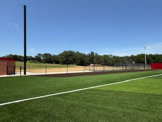 A baseball field with a fence and a brick building in the background.