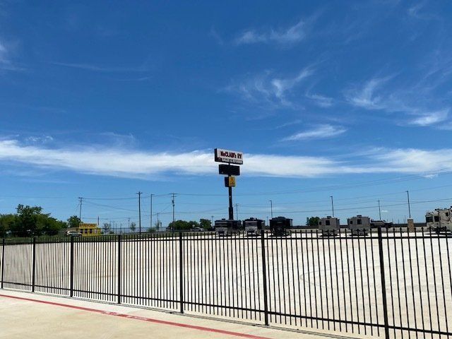 An empty parking lot with a fence and a sign in the background.