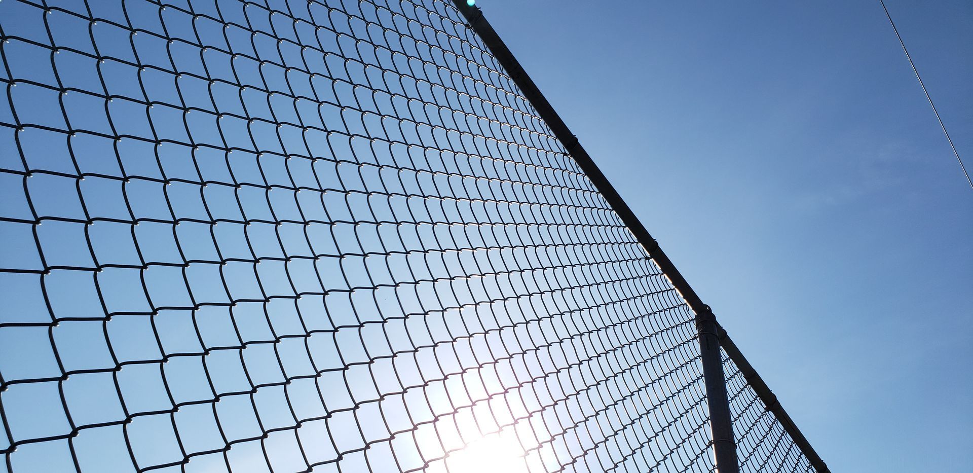 Looking up at a chain link fence with the sun shining through it