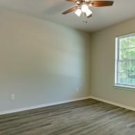 Empty room with wood floors, white walls, ceiling fan, and a window letting in daylight