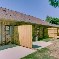 Brick house patio with open wooden privacy panels and a barbecue grill in the yard