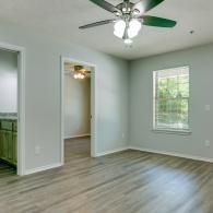 Empty bedroom with gray walls, wood-look floor, ceiling fan, and a window with blinds.