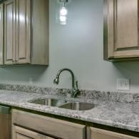 Kitchen sink with granite countertop, wood cabinets, and wall-mounted light fixtures