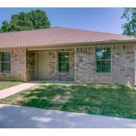 Single-story brick house with a brown roof, front lawn, and walkway.